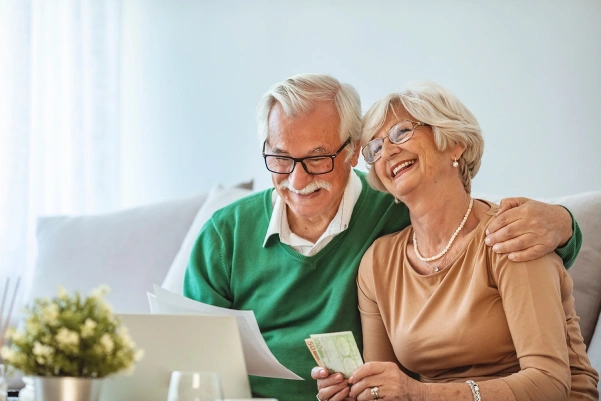 An elderly couple enjoying their time together on a couch, engrossed in using a laptop