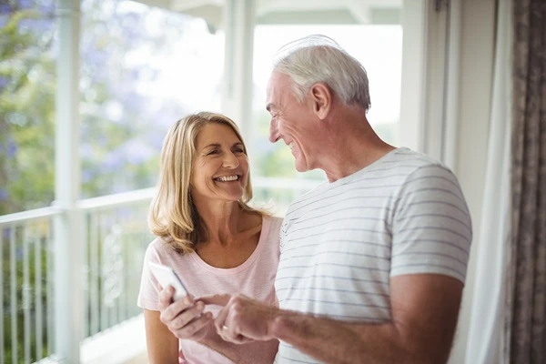 A couple standing by a window, engrossed in their cell phone, sharing a moment of connection.