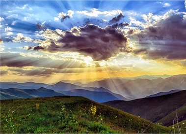 Sunset over majestic mountains with billowing clouds and radiant sunbeams illuminating the breathtaking landscape.