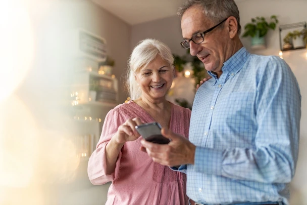 An elderly couple smiling while viewing content on a smartphone together
